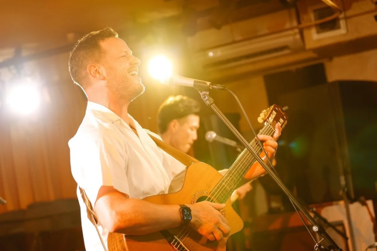 Nelson singing and playing guitar on stage under warm lights